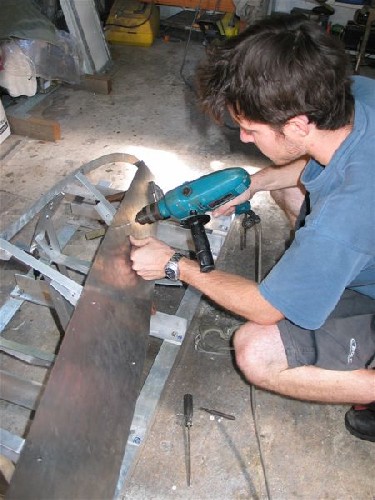 Chris drilling holes to fix metal hull sheeting onto frames